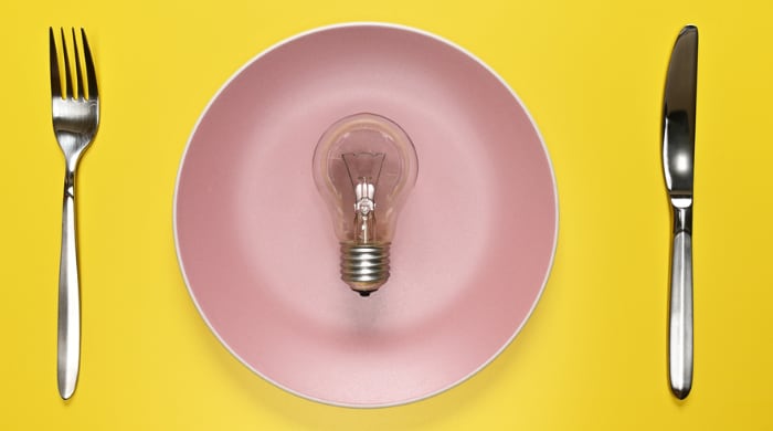Lightbulb on a pink plate set with knife and fork